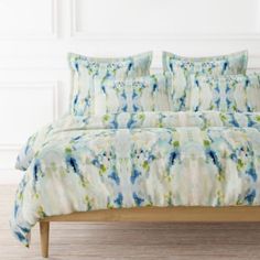 a bed with blue and green comforters on top of it in a white room