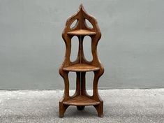 a three tiered wooden shelf sitting on top of a cement floor next to a gray wall