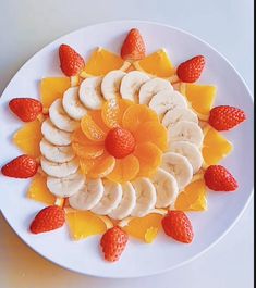 a white plate topped with sliced bananas and oranges next to strawberries on top of each other