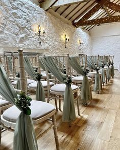 rows of white chairs with green sashes and bows on them in an indoor setting