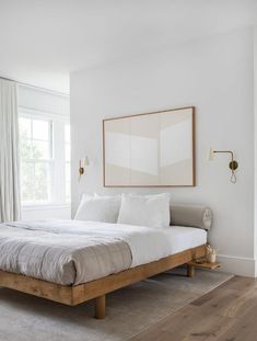 a bedroom with white walls and wood floors, a large bed in the center is flanked by two framed pictures on the wall