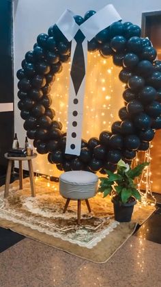 a black and white balloon wreath with a tie on it, surrounded by string lights