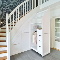 an open closet under the stairs in a room with blue wallpaper and white furniture