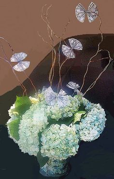 a vase filled with white flowers and butterflies on top of a brown table next to a wall