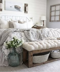 a bed with white sheets and pillows in a bedroom next to a table with baskets on it