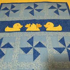 three rubber ducks sitting on top of a blue and yellow quilted table runner with arrows