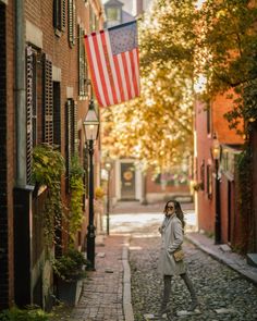 a woman is walking down an alleyway with an american flag hanging from the building