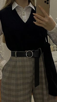 a woman is taking a selfie with her cell phone while wearing a black sweater and plaid pants