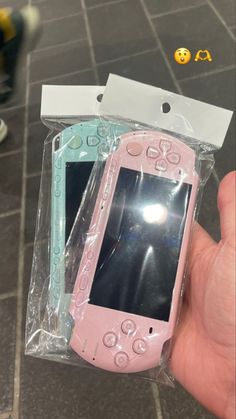 a hand holding a pink and blue cell phone in a plastic bag on the ground