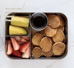 a bento box filled with pancakes, strawberries, and bananas next to a cup of coffee