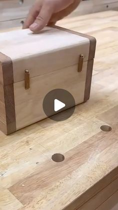 a wooden box sitting on top of a table next to a person's hand