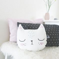 a white cat pillow sitting on top of a bed next to a vase with flowers