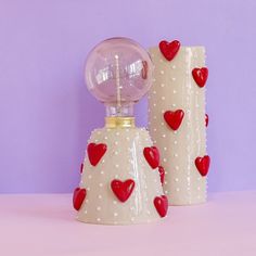 two white vases with red hearts on them sitting next to each other in front of a purple wall