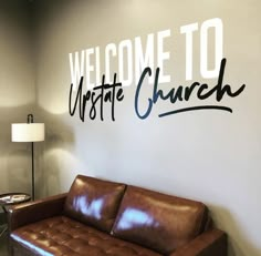 the welcome sign is painted on the wall behind a leather couch