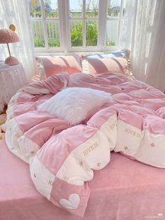 a bed with pink comforter and pillows in a small room next to a window