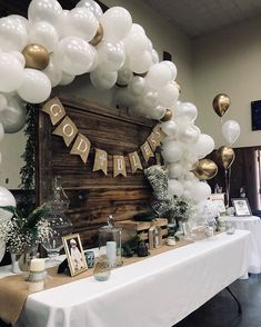 a table topped with balloons and decorations for a baby's first birthday party in white and gold