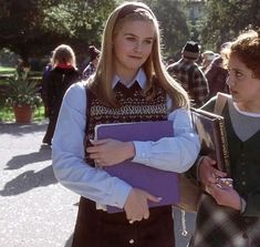 two girls in school uniforms are walking down the street with folders on their laps