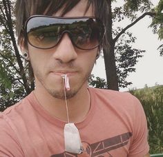 a man wearing sunglasses and chewing on something with a toothbrush in his mouth,