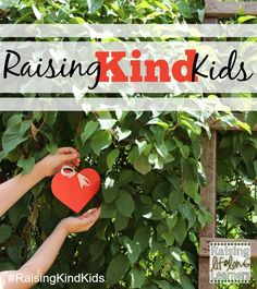 two hands holding a red heart with the words raising kids on it in front of green leaves