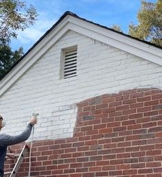 a man is painting the side of a brick building with white paint and a ladder