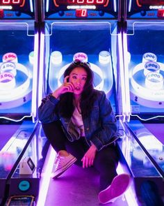 a woman sitting on the ground in front of two slot machines talking on a cell phone