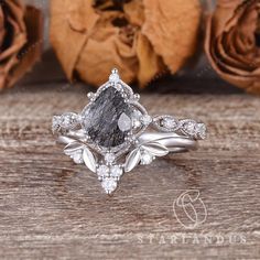 an engagement ring with a pear shaped gray diamond surrounded by leaves and flowers on a wooden surface