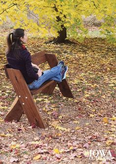 a woman sitting on a wooden bench under a tree with yellow leaves in the background