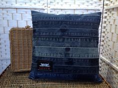 a blue denim pillow sitting on top of a wicker chair next to a woven basket