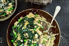 two bowls filled with pasta and vegetables on top of a black table next to silverware