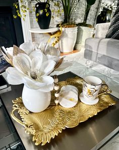 there is a gold tray with white flowers on it and two cups in the middle