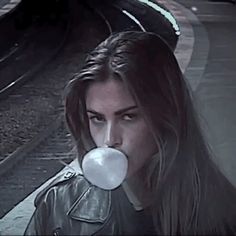 a woman with long hair blowing a bubble in front of her face while standing on train tracks