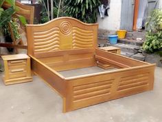 a wooden bed frame sitting on top of a cement floor next to potted plants