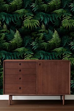 a wooden cabinet sitting in front of a wall with green leaves on it and a plant behind it