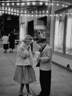 a man standing next to a woman on the street while holding a cup of coffee