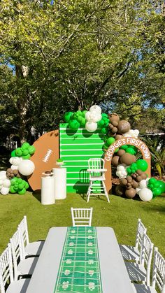 a football themed party with green and white balloons on the wall, tables and chairs