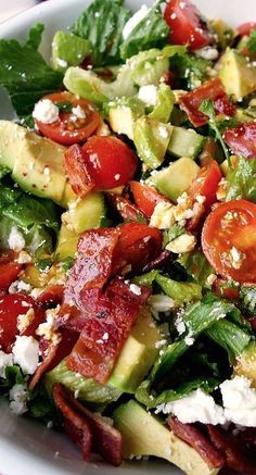 a salad with tomatoes, cucumbers, cheese and lettuce in a white bowl