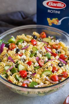 a glass bowl filled with pasta salad next to a carton of rotini