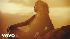 a woman sitting on top of a rock next to a sky filled with white clouds