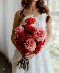 a woman in a white dress holding a bouquet of red and pink flowers on her wedding day