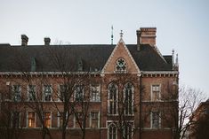 an old brick building with many windows and trees in the foreground, on a cloudy day