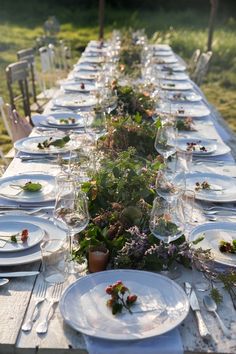 a long table is set with white plates and silverware for an outdoor dinner party