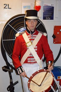 a man in uniform is holding a drum and wearing a red jacket with white pants