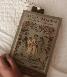 a little women book is being held up by someone's hand on a bed