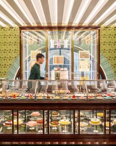 a man standing in front of a display case filled with lots of cakes and pastries