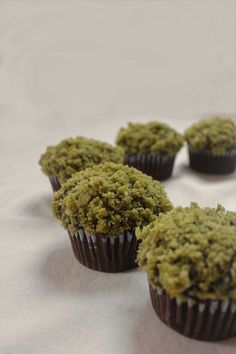 four cupcakes covered in green crumbs sitting on a white table cloth