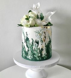 a green and white cake with flowers on top sitting on a table next to a wall