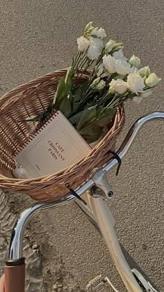 a basket on the back of a bicycle with flowers in it and a book sitting inside