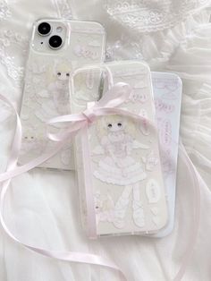 two cell phones sitting next to each other on top of a white sheet with pink ribbon