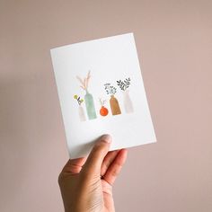 a hand holding up a card with flowers in bottles on it and the bottom one is white