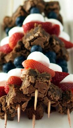 desserts are arranged on sticks with strawberries and blueberries